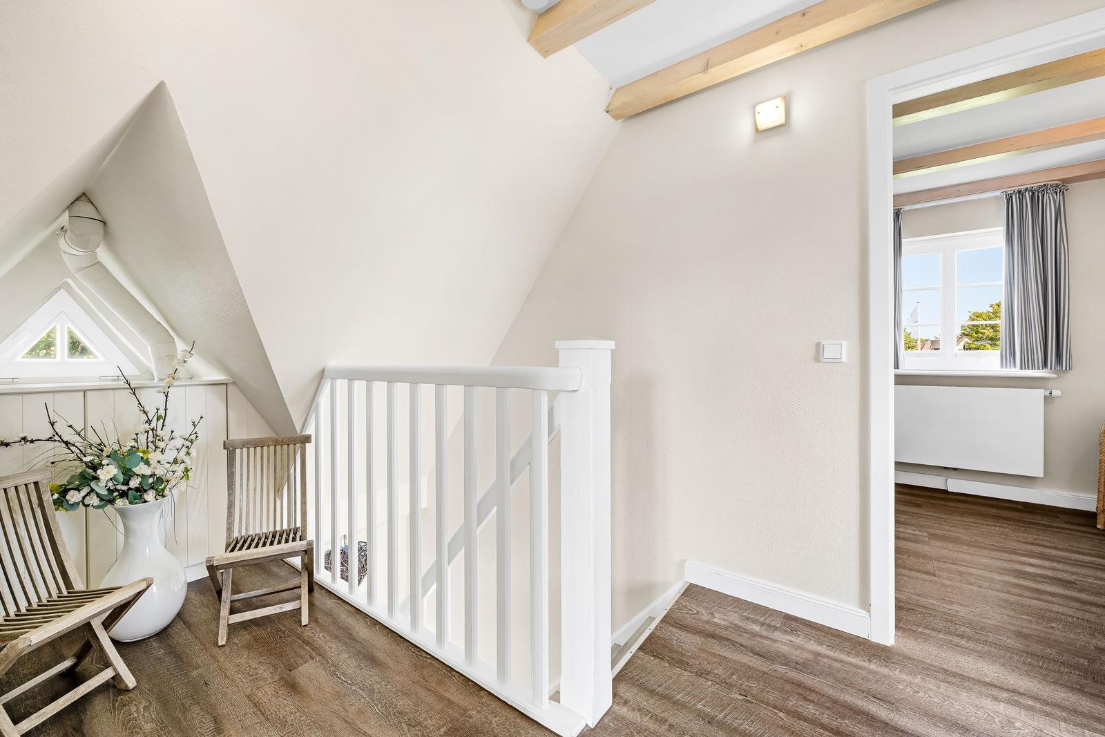 Attic with wooden floors, white railing, and chair. Window with curtains.