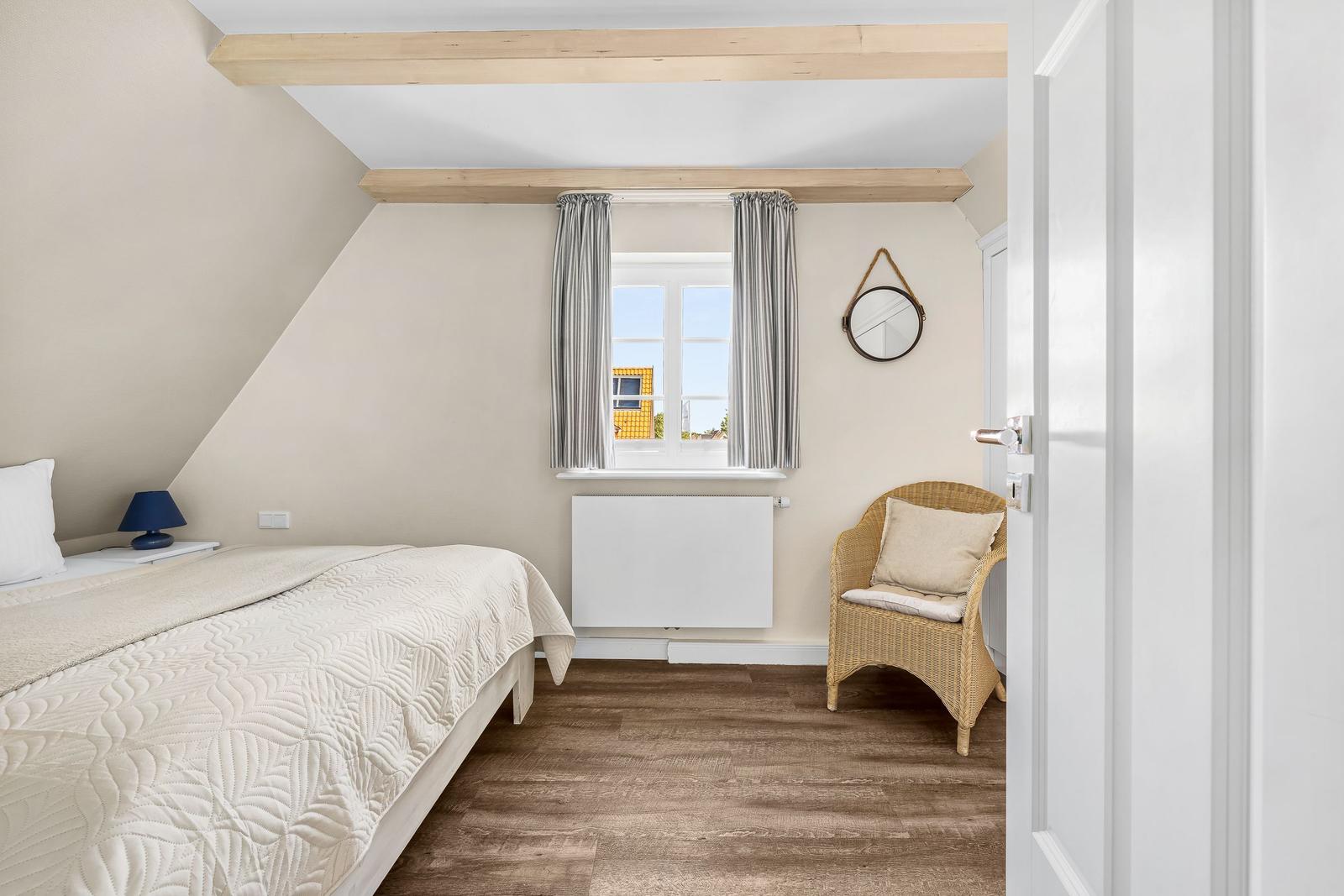 Bedroom with bed, wicker chair, and window with curtains.