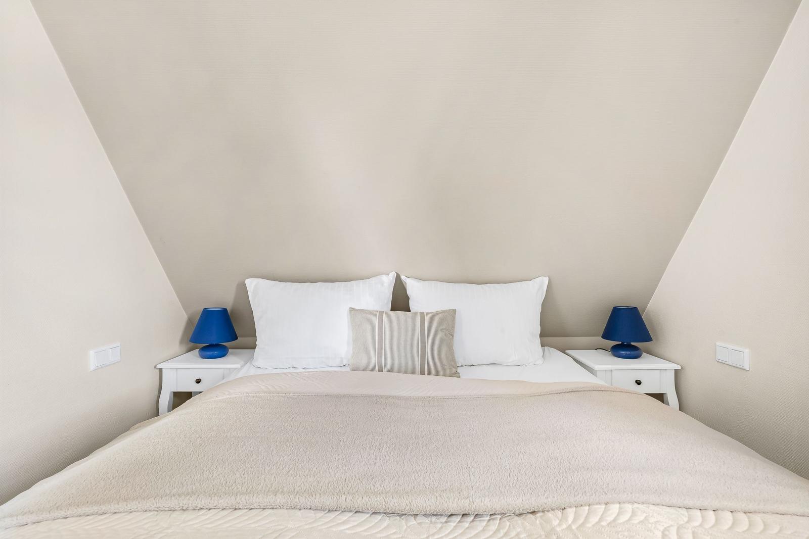 Bedroom with sloped ceiling, white bed, and two nightstands with blue lamps.