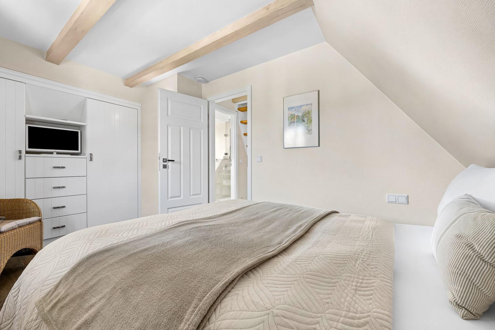 Bedroom with sloped ceiling, bed, wardrobe, and TV.