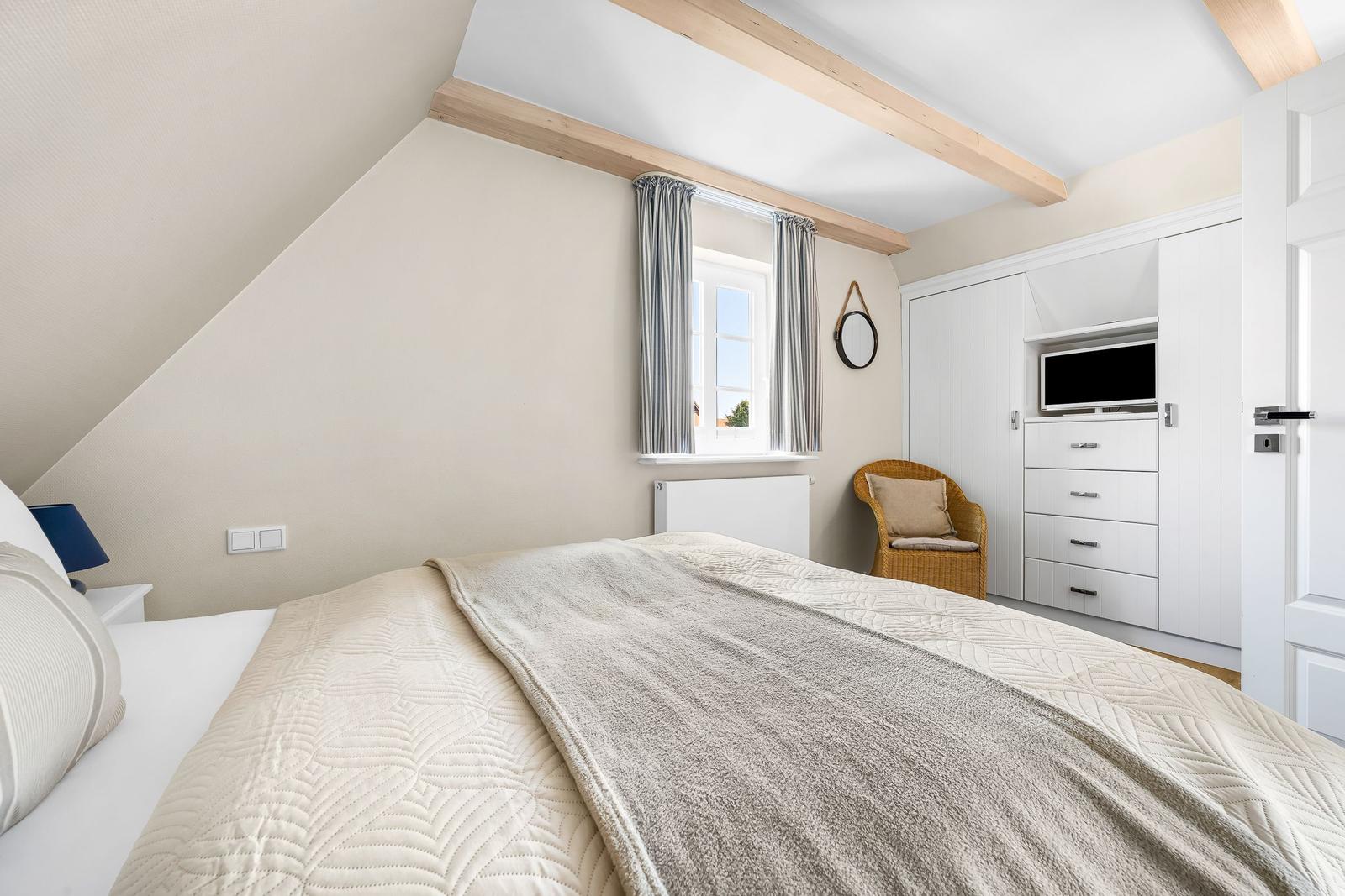 Bedroom with sloped ceiling, bed, wardrobe, and chair.