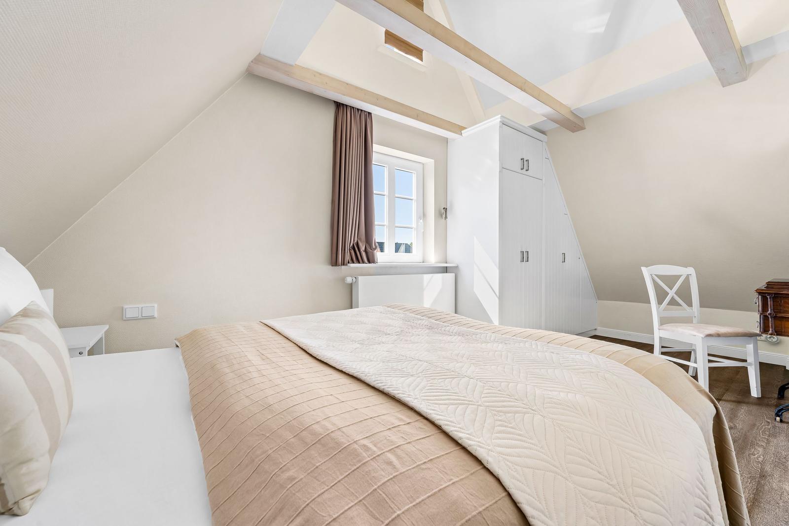 Bedroom with sloped ceiling, window, bed, and wardrobe.