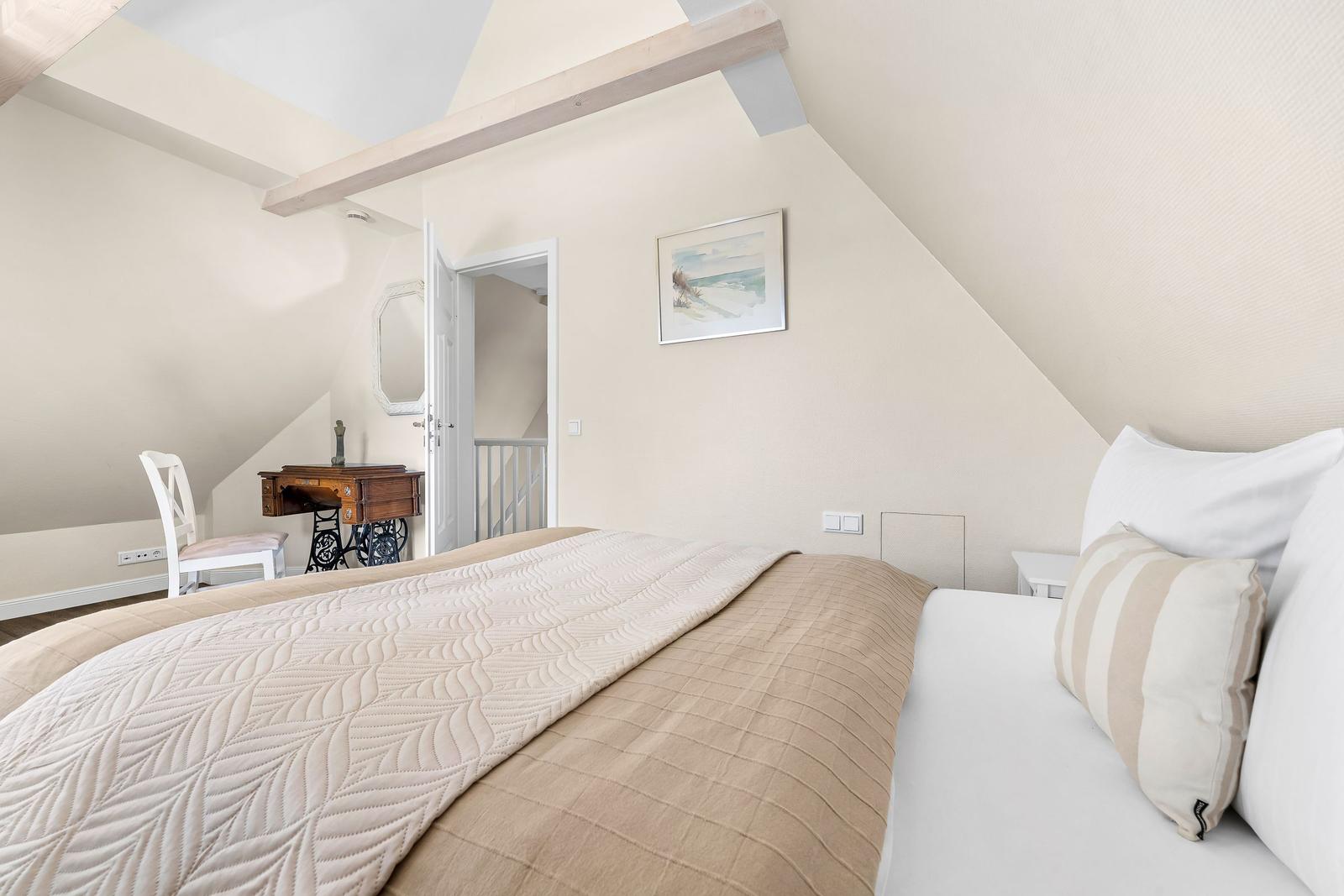 Bedroom with sloped ceiling, bed, desk, and wall picture.