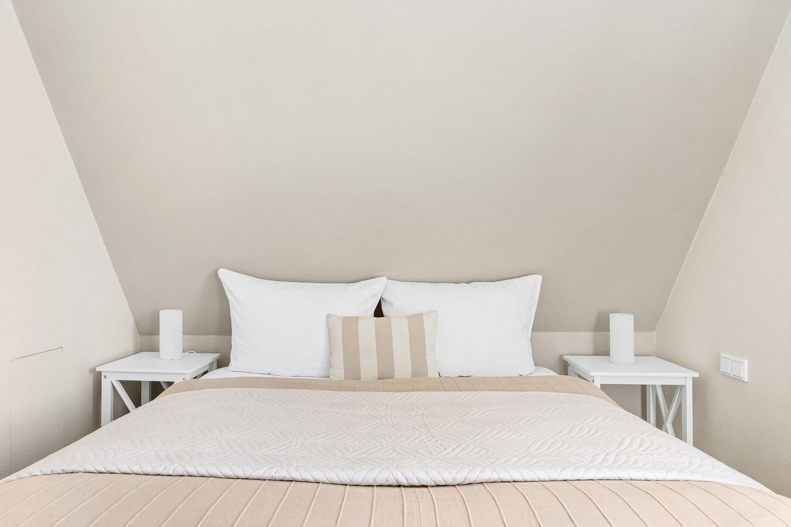 Bedroom with bed, two nightstands, and pillows under sloped walls.