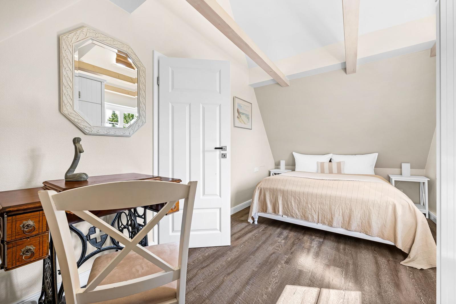 Bedroom with bed, desk, and mirror under wooden beam ceiling.
