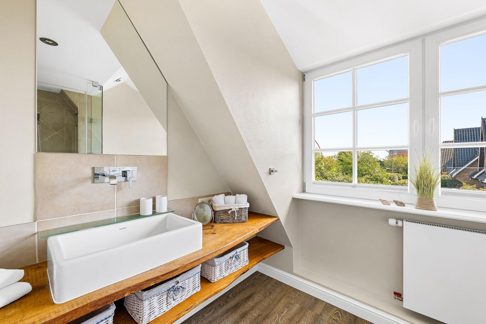 Bathroom with wooden washbasin, mirror, and window with view of green areas.