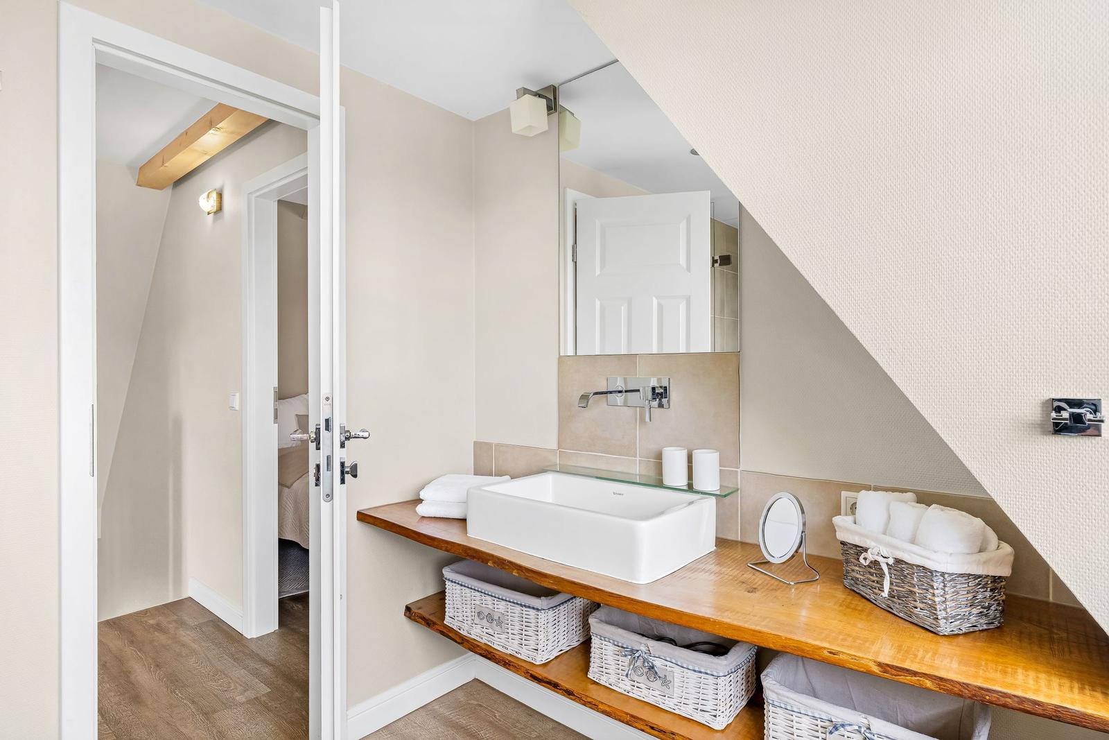 Bathroom with sink, mirror, and baskets. Door leads to bedroom.