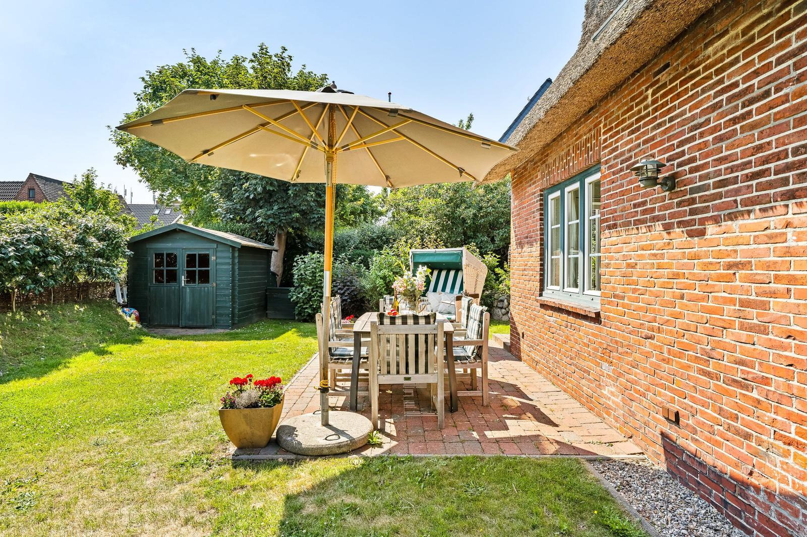 Terrace with table, chairs, and umbrella next to red brick house.