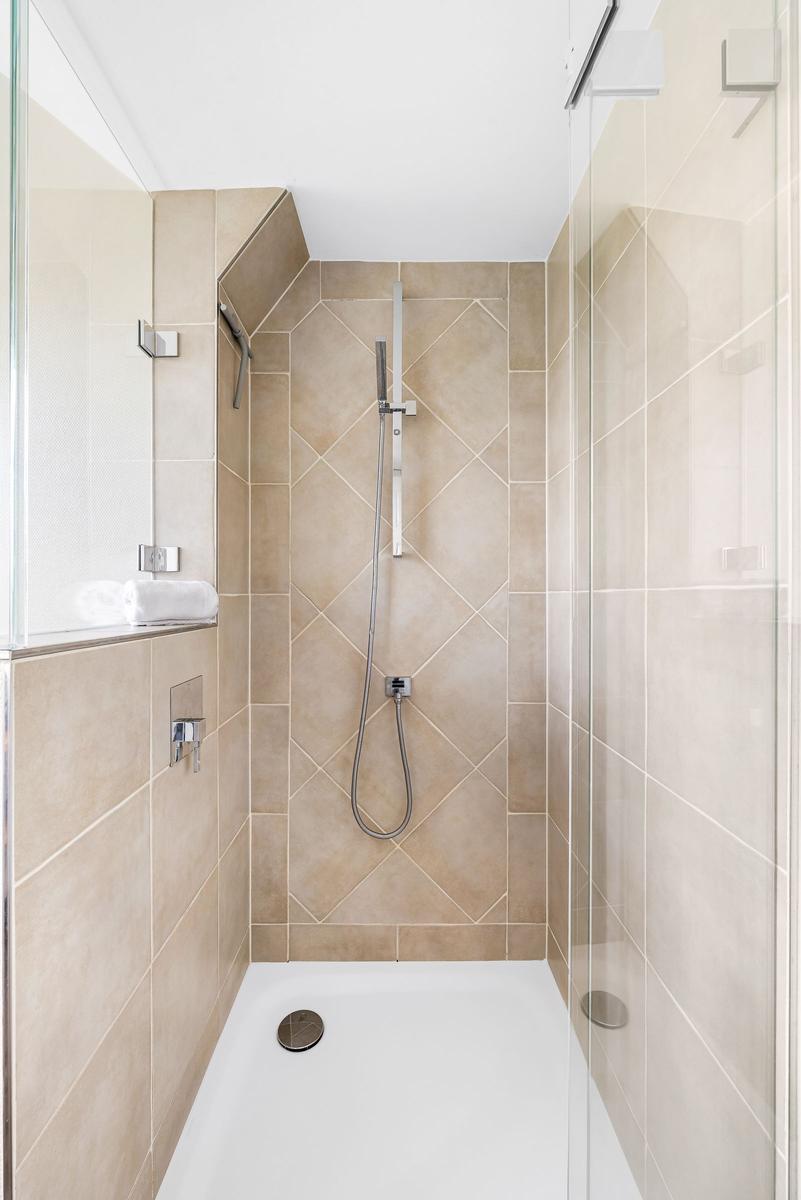 Shower with glass enclosure, beige tiles, and handheld shower.