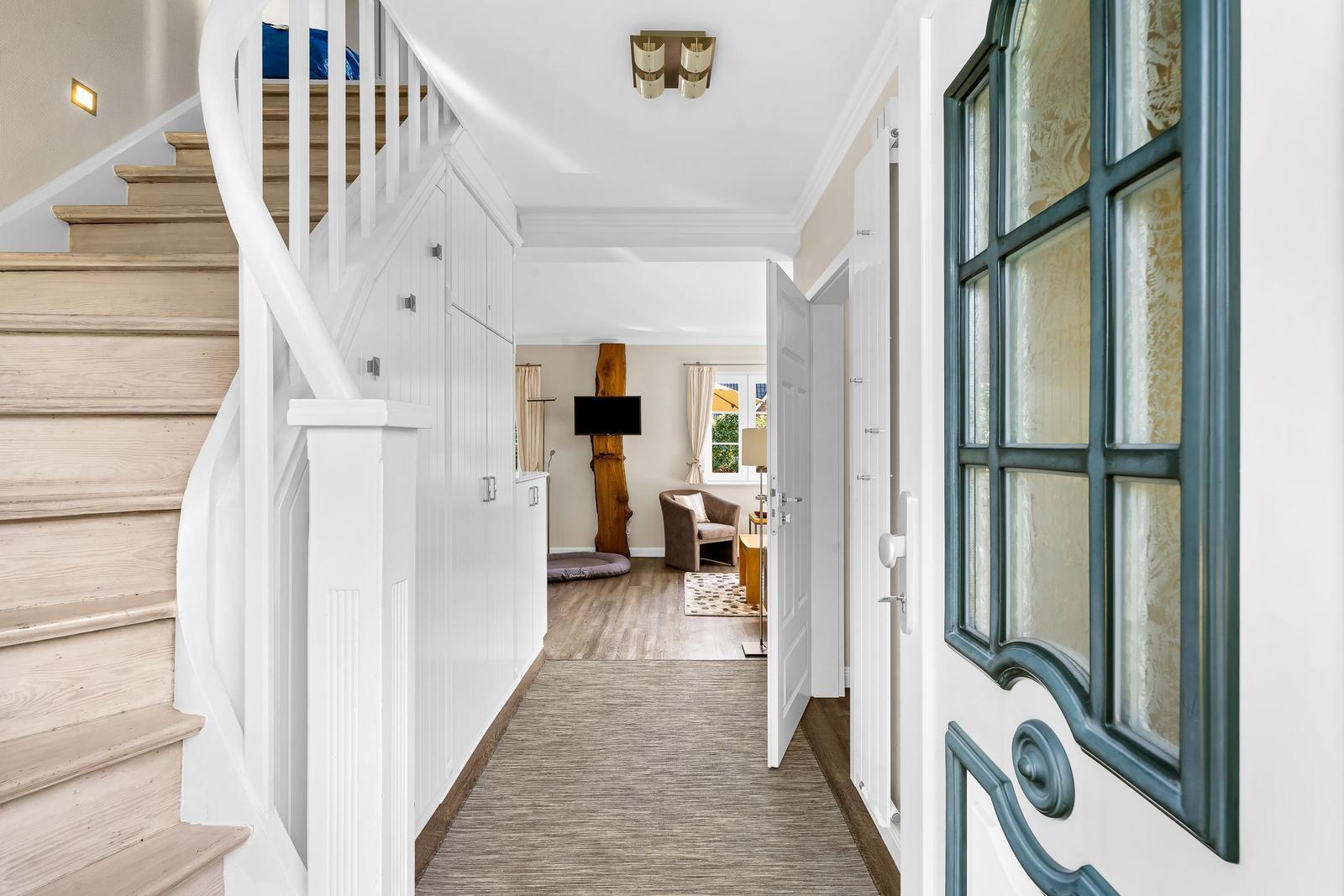 Hallway with staircase and view into living room with armchair and TV.