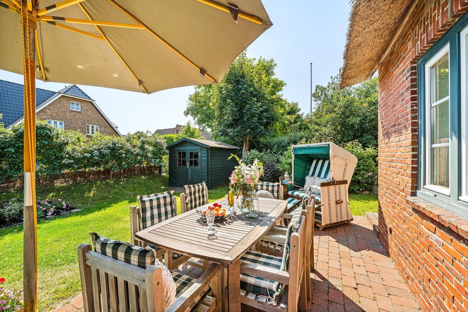 Terrace with table, chairs, and umbrella next to a red brick house.