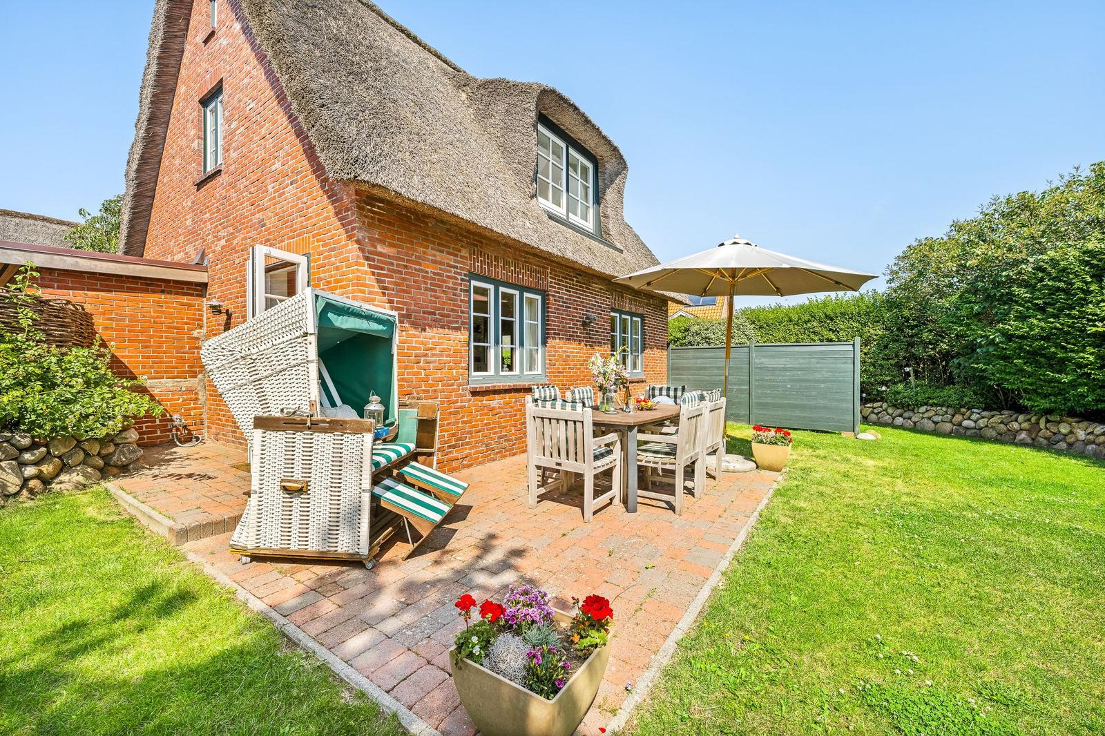 House with thatched roof, terrace with table, chairs, and umbrella.