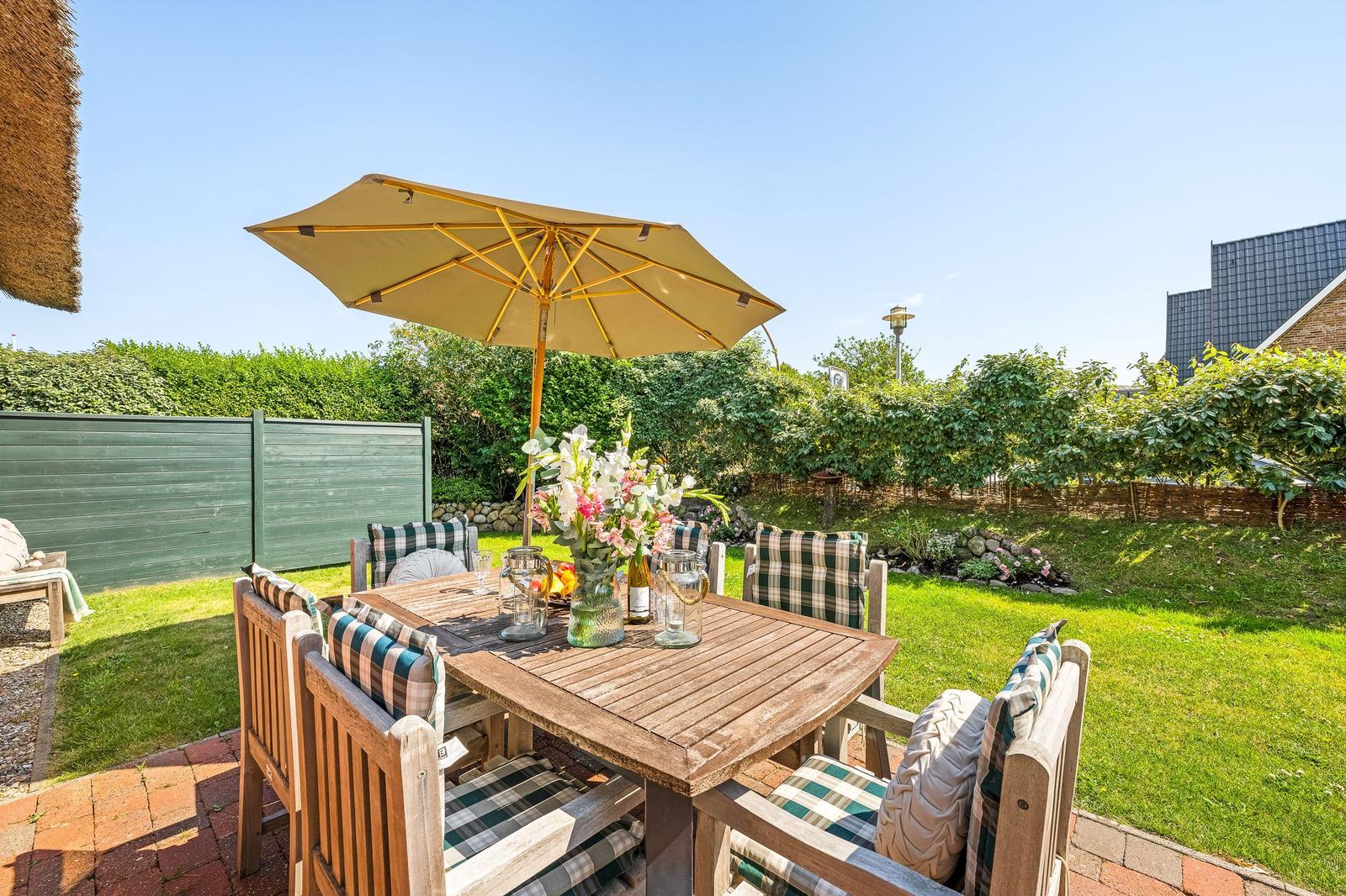 Wooden table with chairs and umbrella in the garden. Green lawn and hedge in the background.