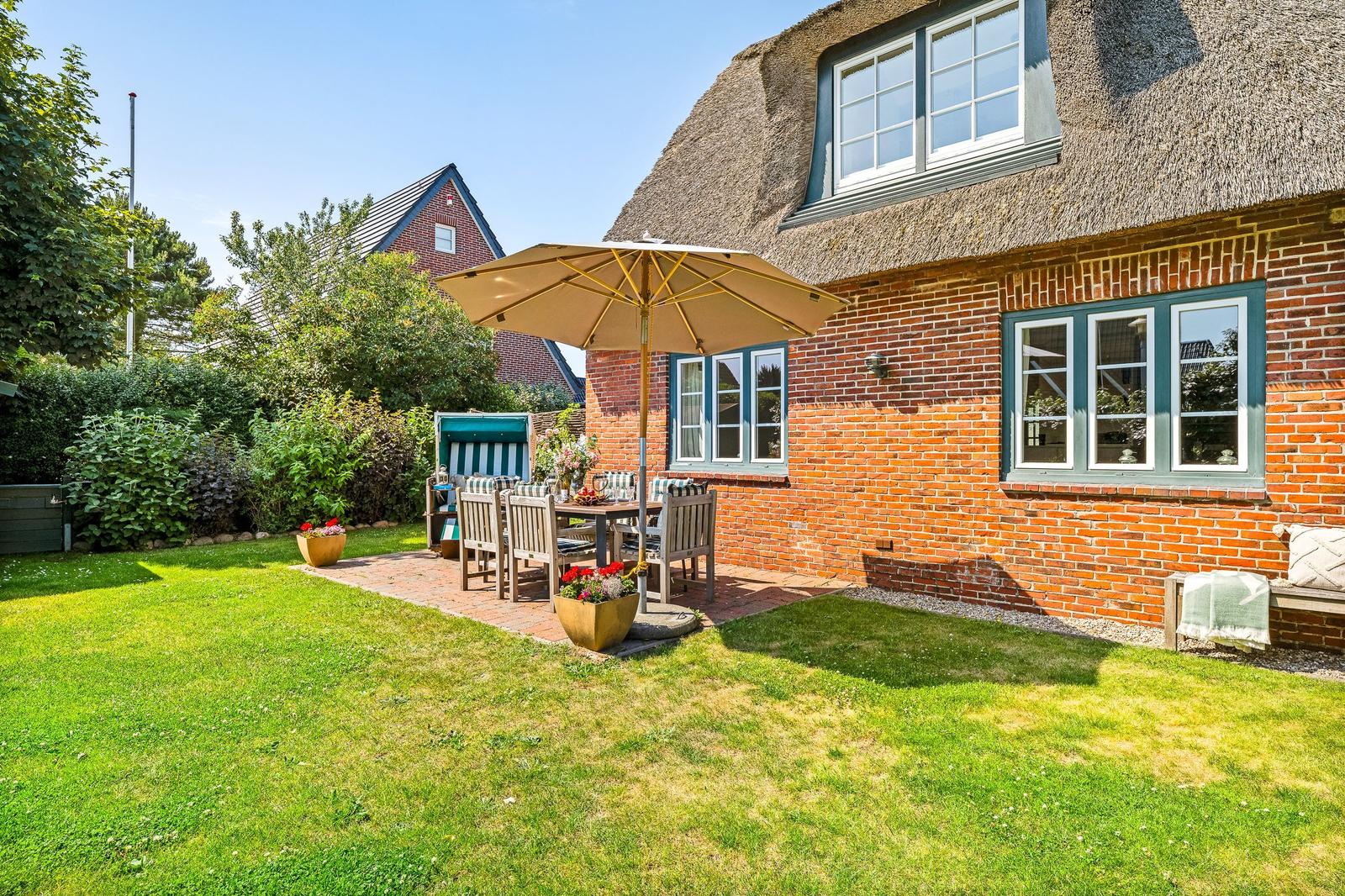 House with thatched roof and garden with table, chairs, and umbrella.