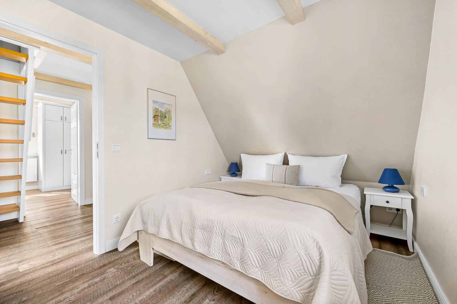 Bedroom with bed, nightstands, and wooden beams. Passage to stairs and wardrobe.