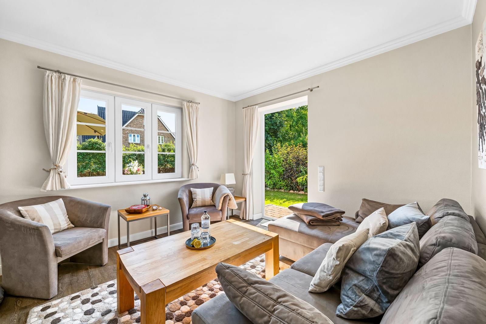 Living room with sofa, armchairs, table, and view of garden and street.