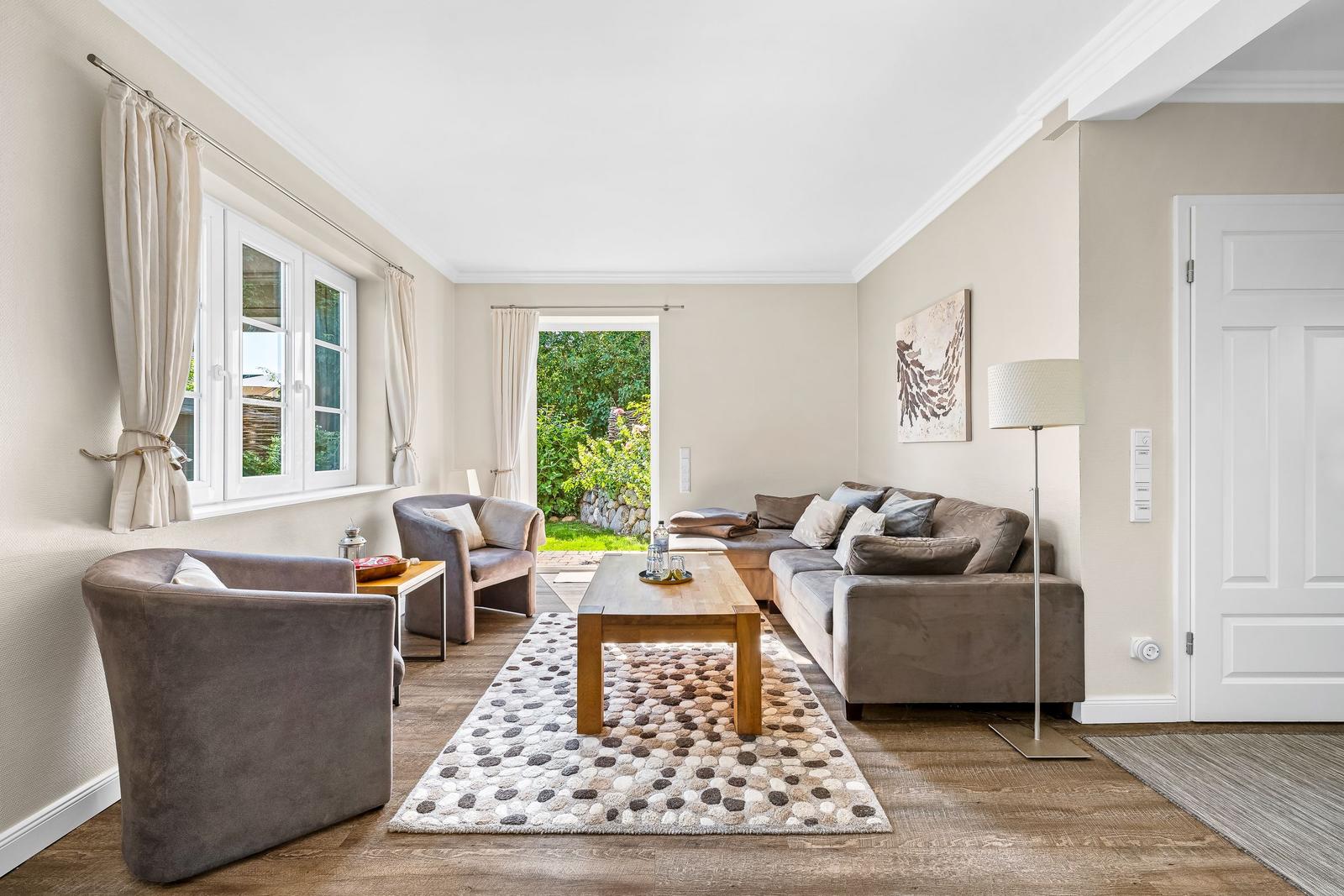 Living room with sofa, armchairs, table, and view of the garden.