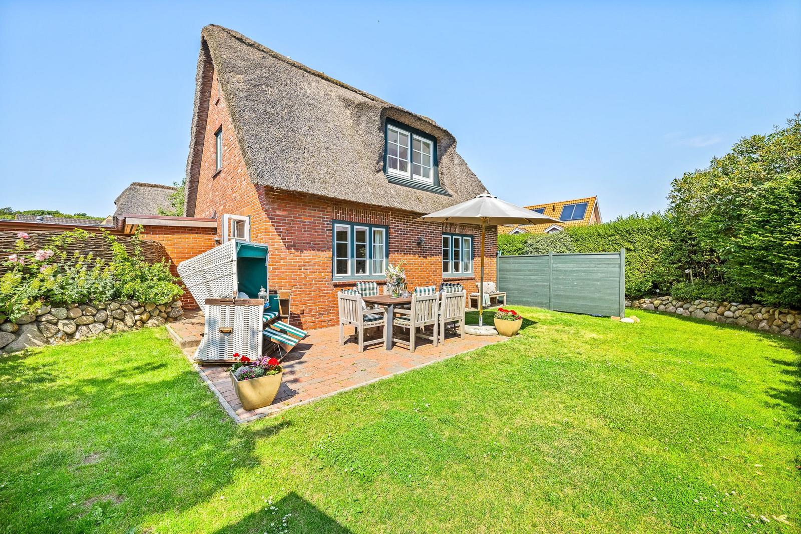 Red brick building with thatched roof and garden area with table, chairs, and umbrella.