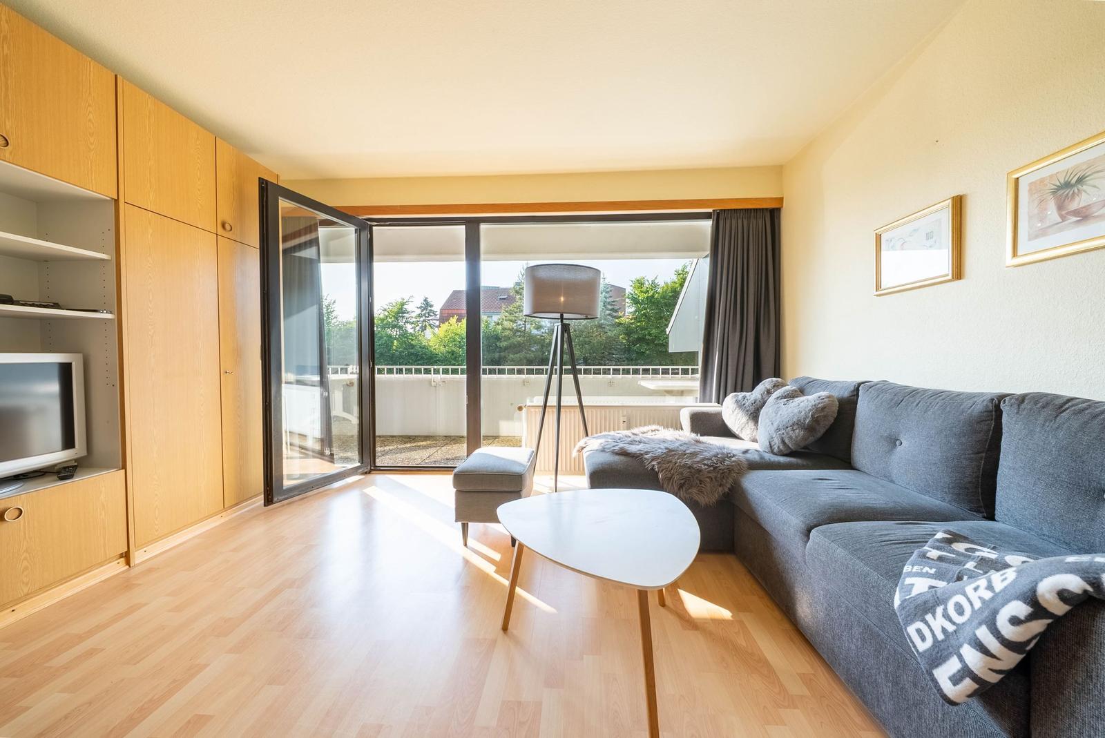 Wohnzimmer mit Sofa, Couchtisch und Balkontür. Holzdielenboden und eingebaute Schränke.