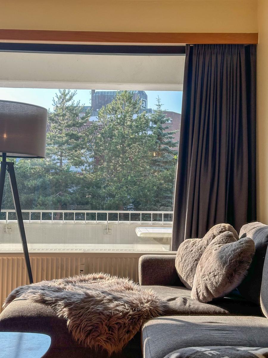 Ein Sofa mit Felldecke und Kissen vor einem Fenster mit Blick auf Bäume.