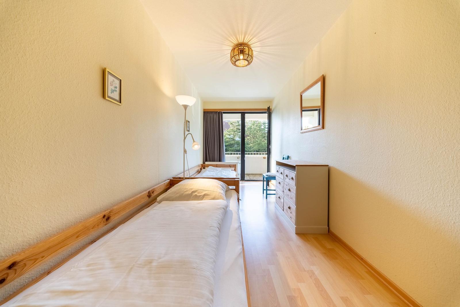 Schlafzimmer mit zwei Betten, Holzboden und Blick auf Balkon.