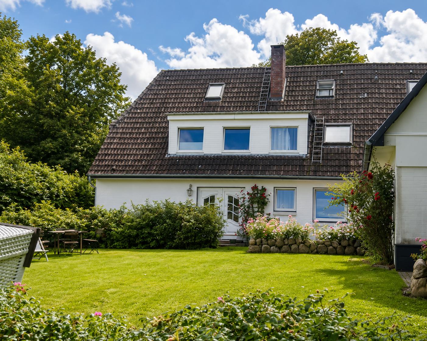 Haus mit Garten, Terrasse und Blumenbeete unter blauem Himmel.
