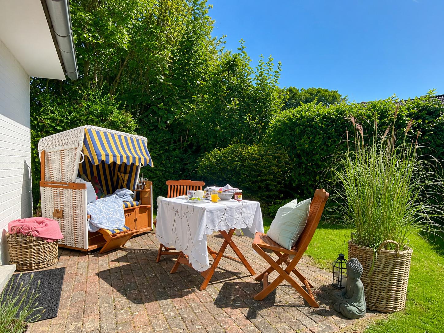 Hinterhof mit Strandkorb, Tisch und Stühlen, Grünflächen und Pflanzen.