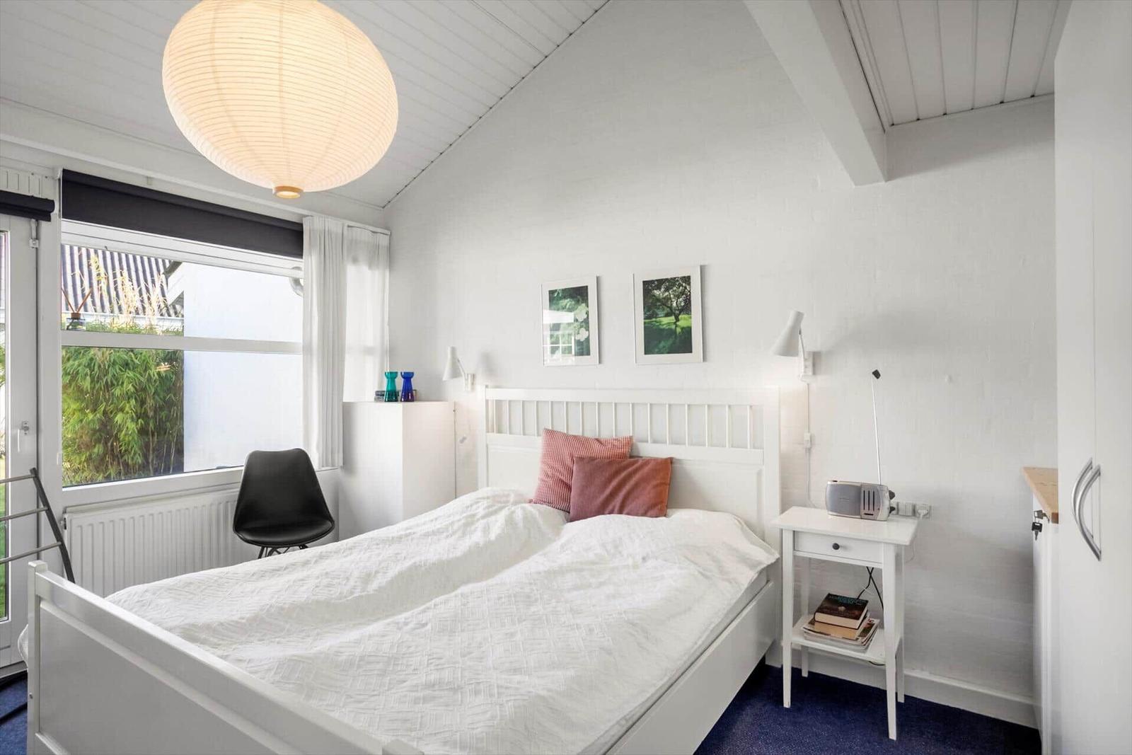 Schlafzimmer mit weißem Bett, Fenster und Deckenleuchte.