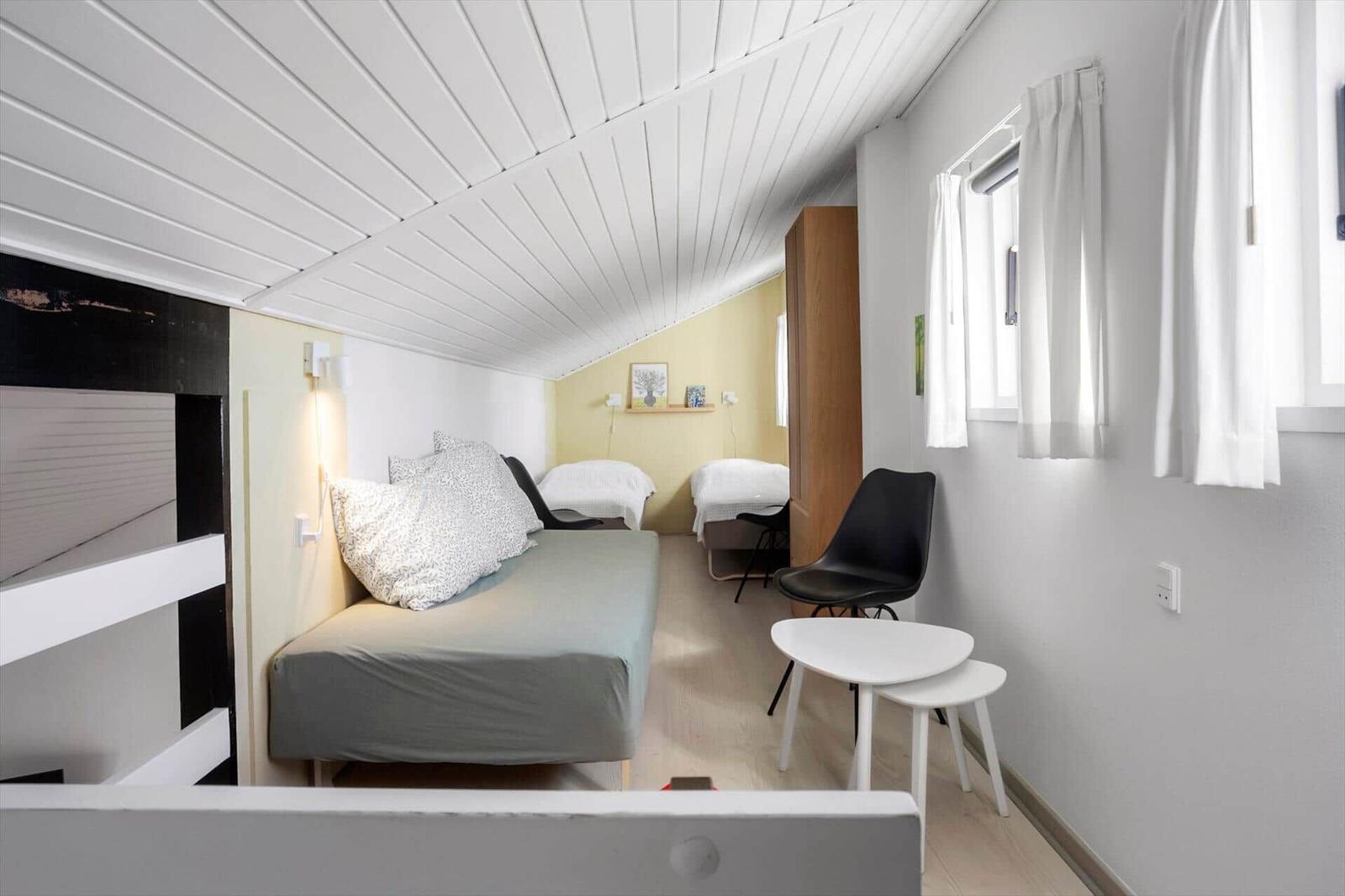 Schlafzimmer mit zwei Betten, Stuhl und Tisch unter schrägem Dach