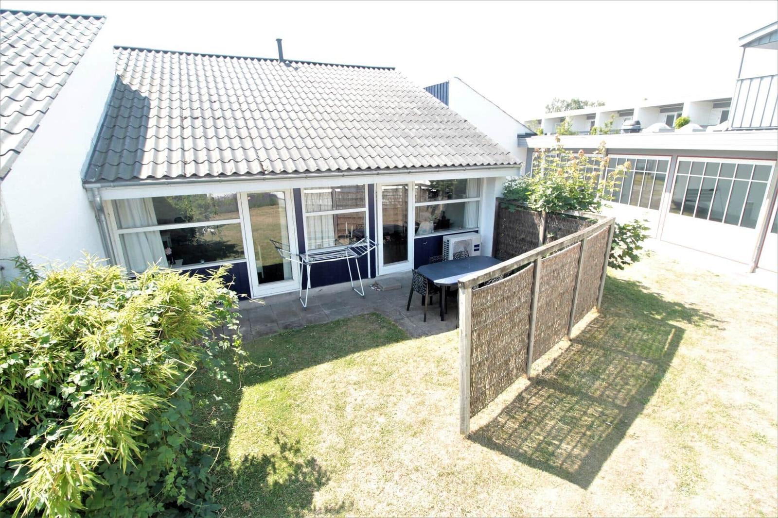 Haus mit Garten, Terrasse und Sitzgelegenheiten. Holzzaun und Pflanzen umgeben den Außenbereich.