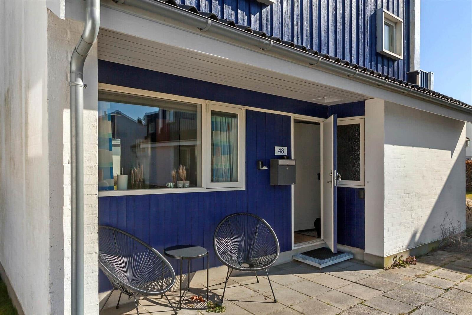 Blau gestrichene Fassade mit Terrasse, zwei Stühlen und Tisch vor der Tür.