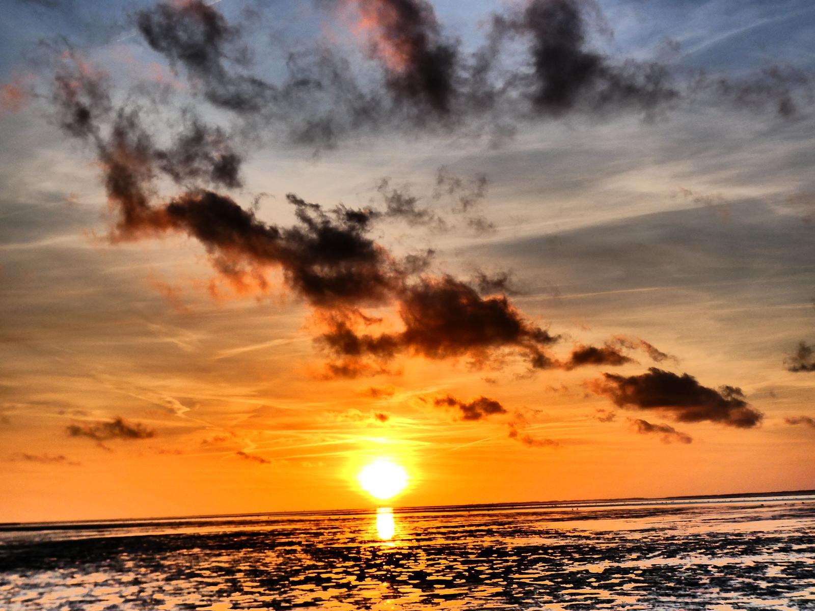 Sonnenuntergang über Wasser mit orangefarbenem Himmel und dunklen Wolken.