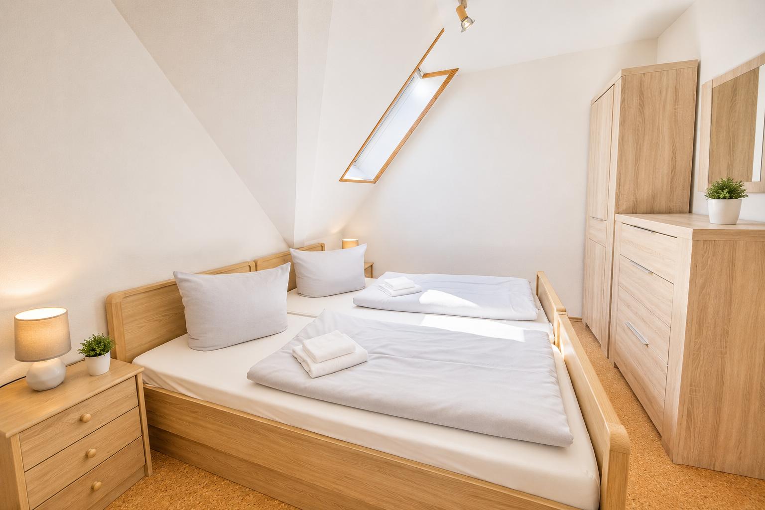 Schlafzimmer mit Doppelbett, Schrank und Nachttisch. Dachfenster und Holzmöbel.