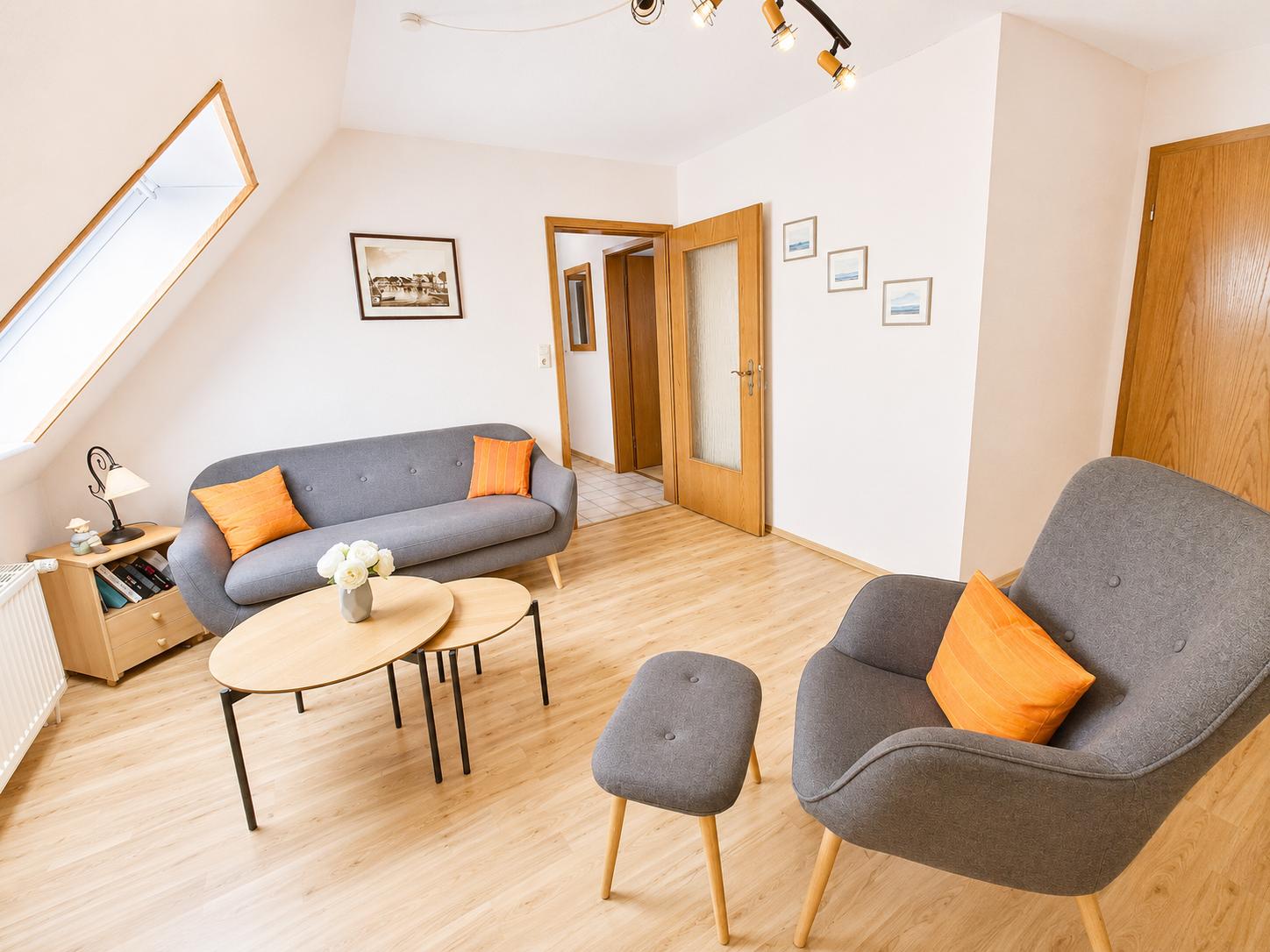 Wohnzimmer mit grauem Sofa und Sessel, Holzboden und Dachfenster.