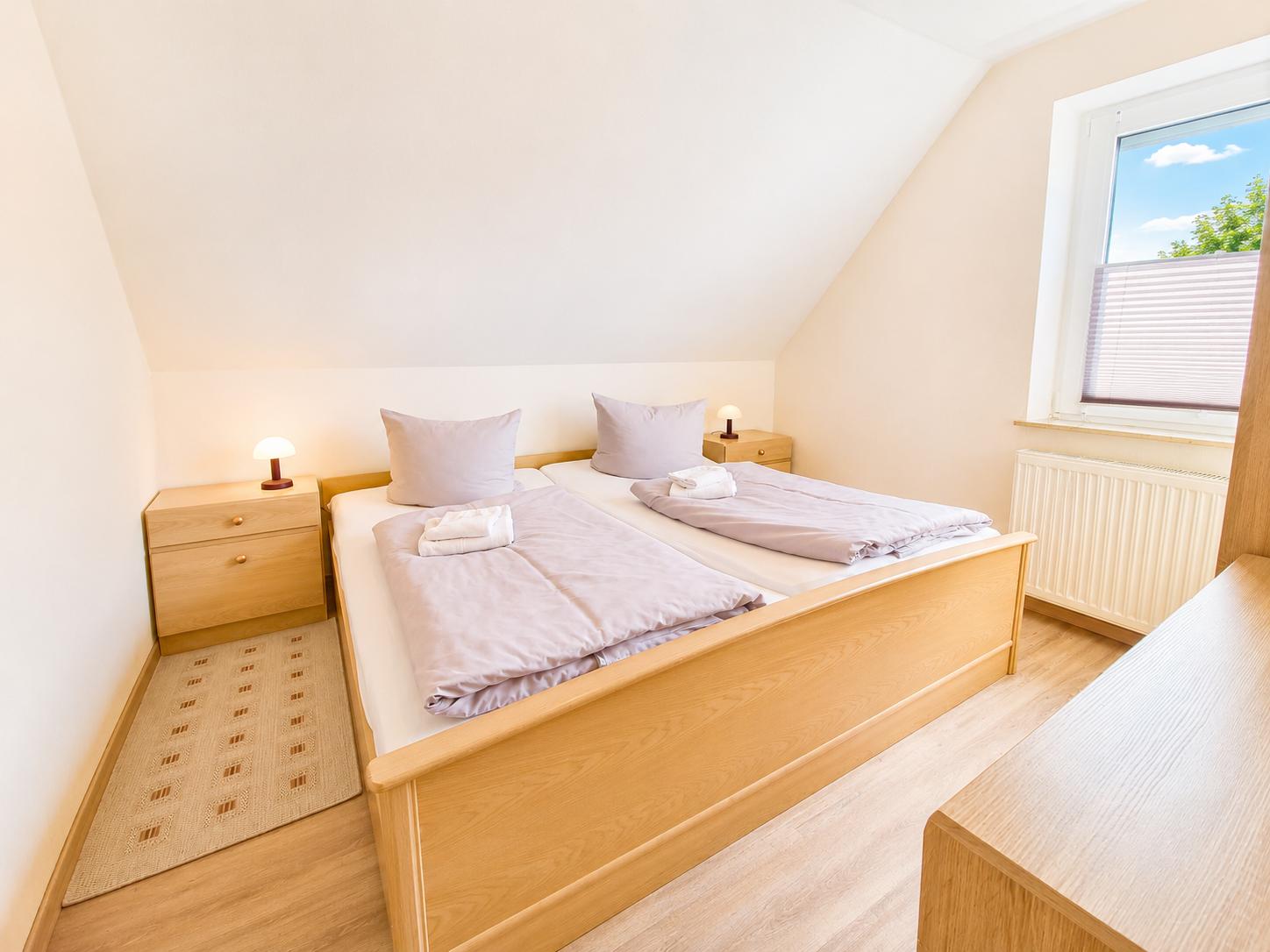 Zimmer mit Doppelbett, Nachttischen und Fenster mit Blick nach draußen.