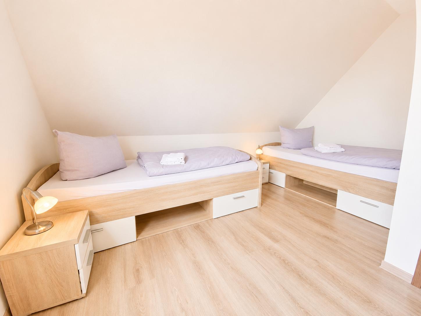 Zwei Einzelbetten mit Nachttischen und Lampen in einem Dachgeschosszimmer mit Holzboden.
