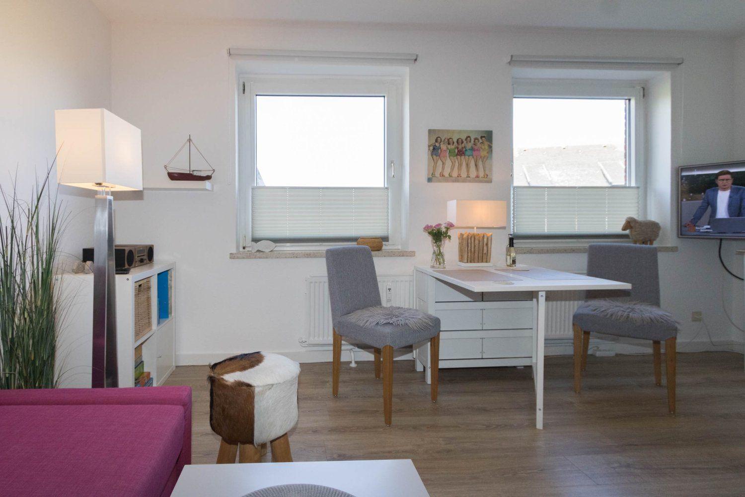 A room with a table, two chairs, windows, and a TV. A sofa and a lamp are visible.