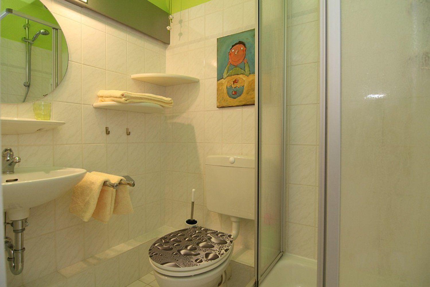 Bathroom with shower, toilet, sink, and mirror. Wall art and towels are present.