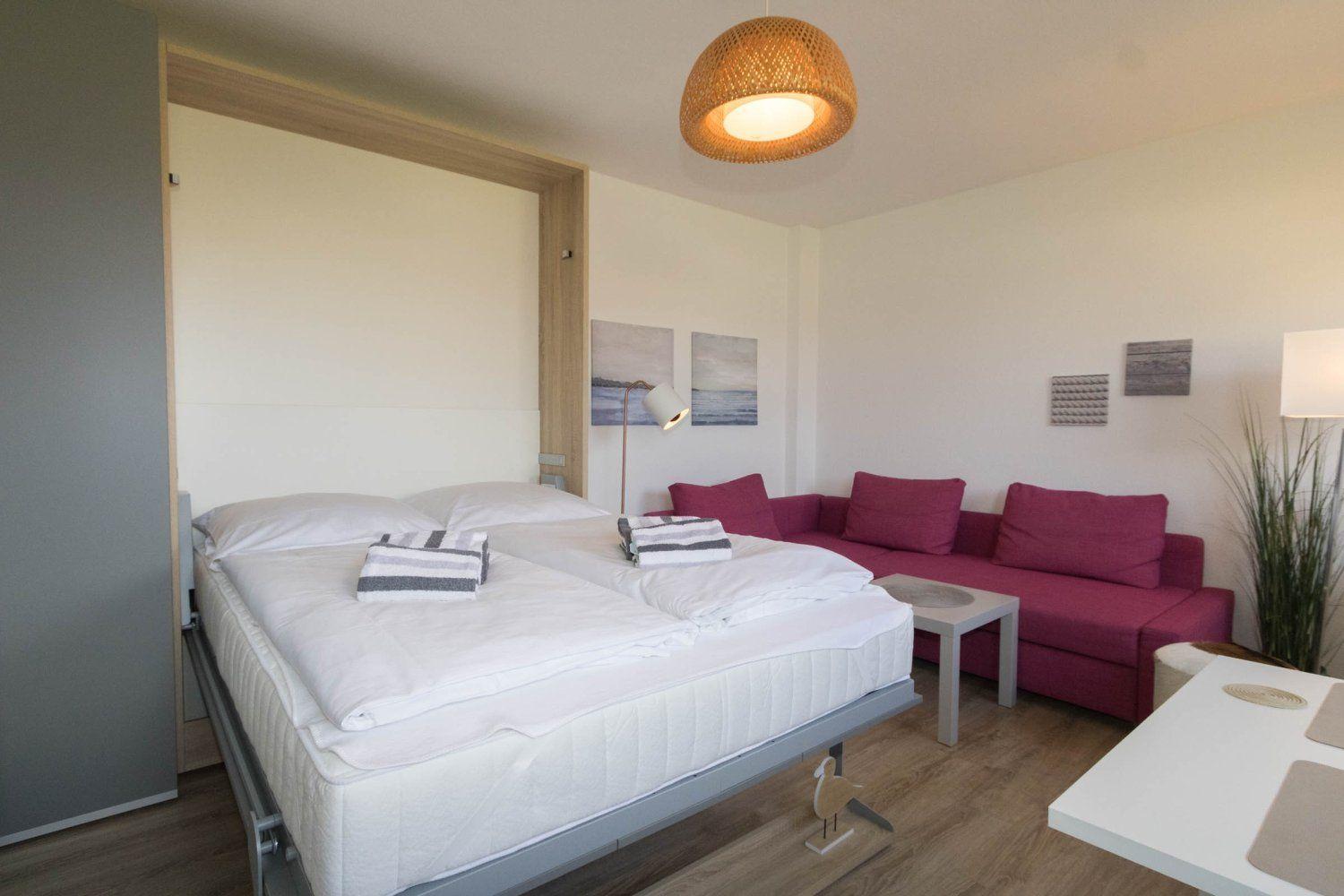 Bedroom with bed, sofa, and table. Ceiling light and wall art visible.