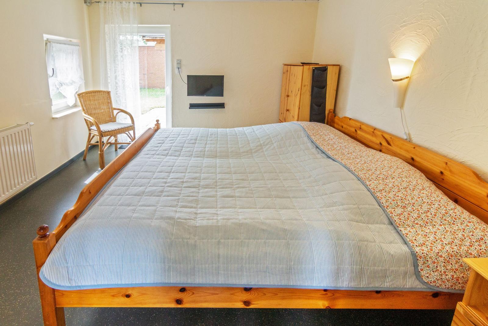 Ein Schlafzimmer mit großem Bett, Fernseher, Schrank und Stuhl vor Fenster.