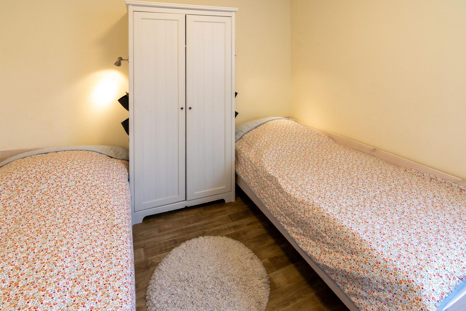 Zwei Betten mit Blumenbezug, weißer Schrank und runder Teppich im Raum.