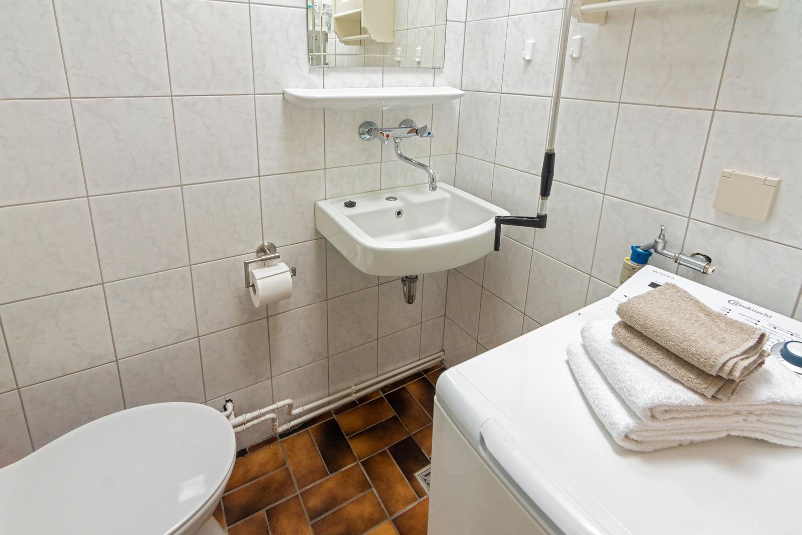 Badezimmer mit Toilette, Waschbecken und Wäschetrockner mit Handtüchern.