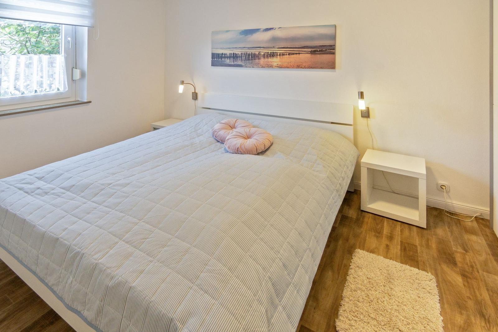 Schlafzimmer mit Bett, Fenster und Wandbild. Holzboden und zwei Nachttische.