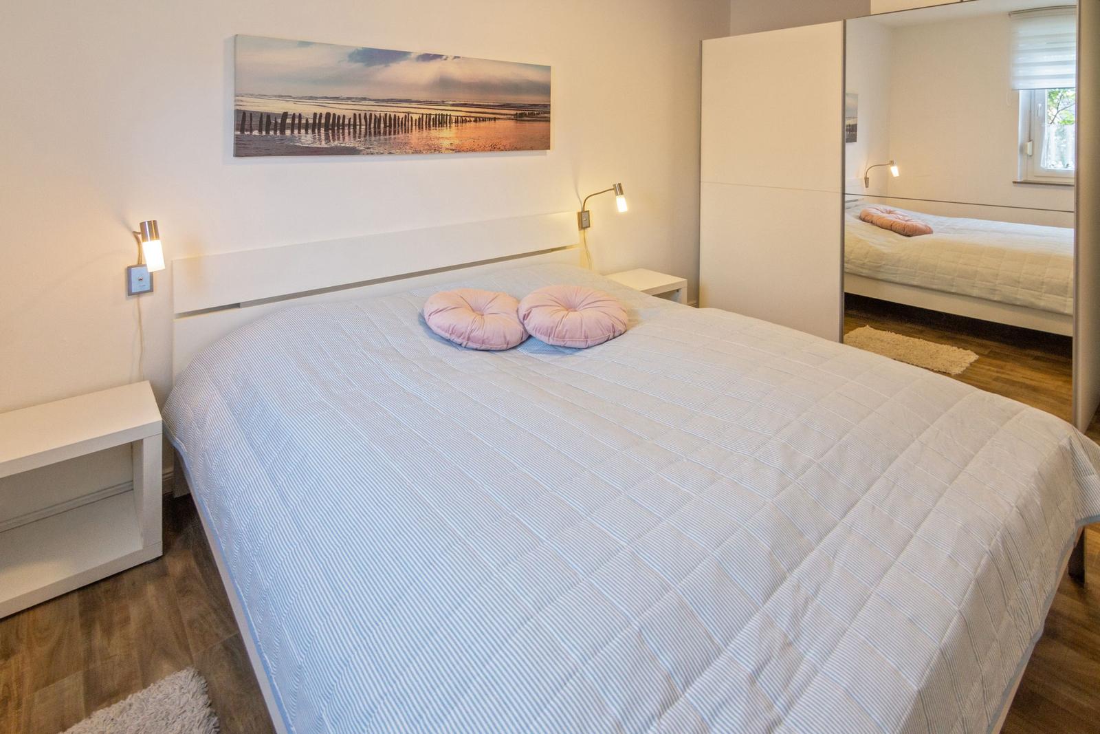 Schlafzimmer mit Bett, Nachttischen und Spiegelschrank. Wandbild über dem Bett.