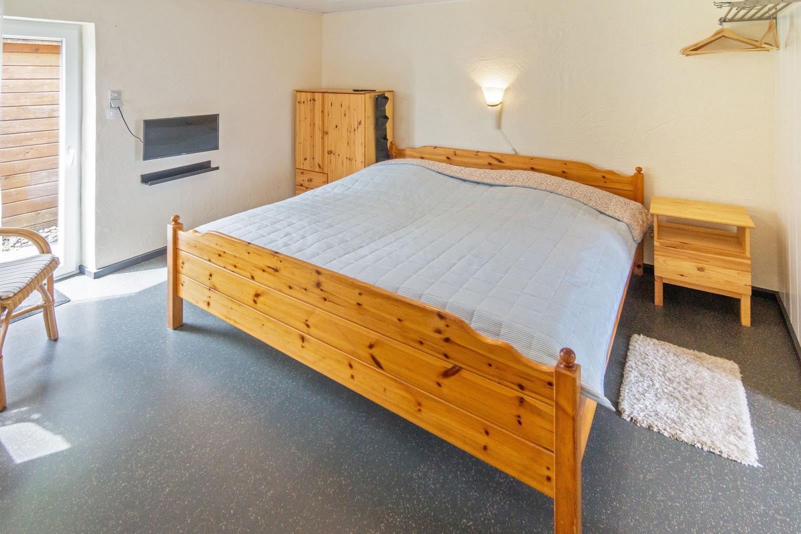 Schlafzimmer mit Holzbett, Kleiderschrank und Nachttisch. Tür zum Außenbereich.