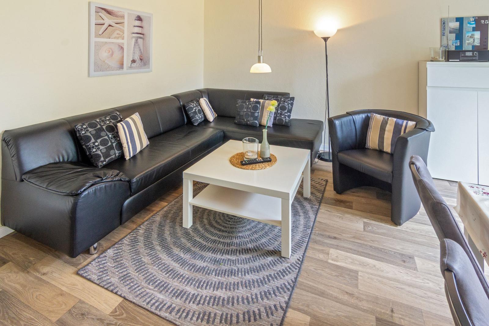 Ein Wohnzimmer mit schwarzer Ledercouch, weißem Tisch und Teppich auf Holzboden.