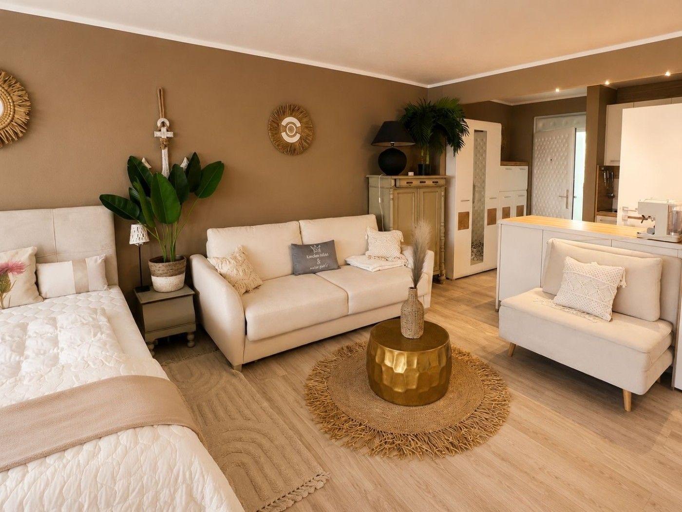 Ein Wohnzimmer mit Sofa, Sessel und Bett. Holzboden und goldener Couchtisch.