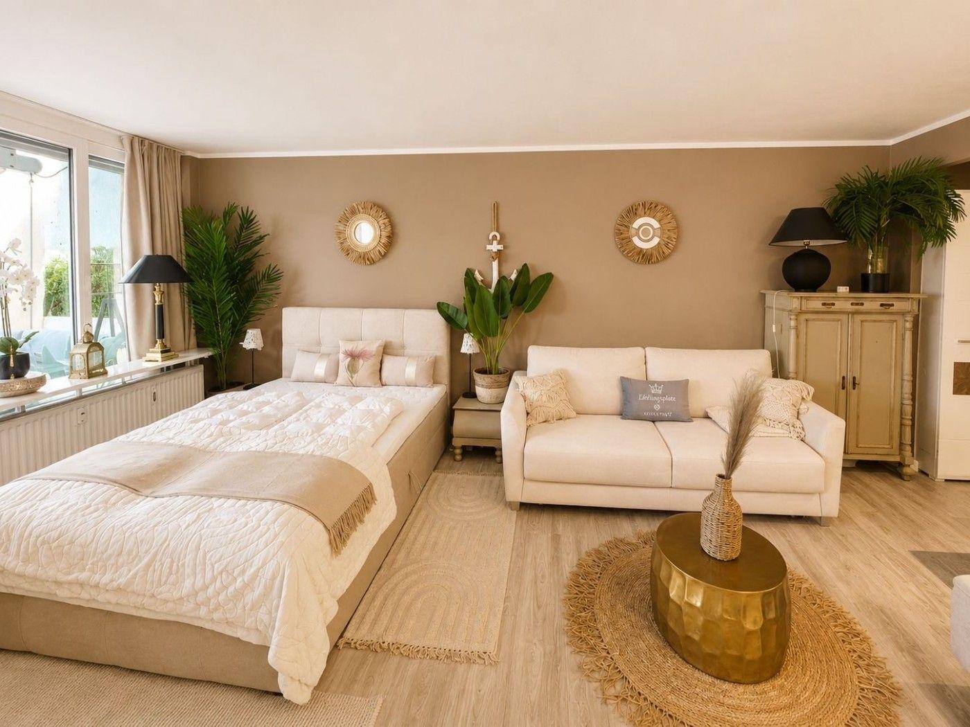Schlafzimmer mit Sofa, Bett und Pflanzen. Holzboden und beige Wand.