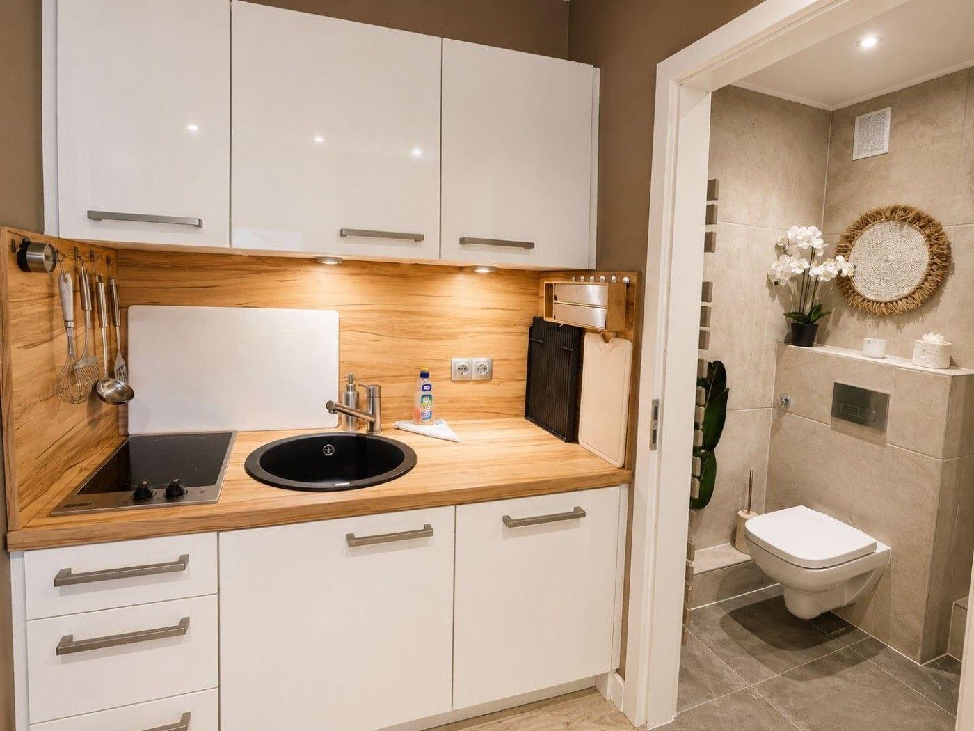 Küche mit weißen Schränken, Holz Arbeitsplatte und integriertem Spülbecken. Neben dem Bad mit Toilette.