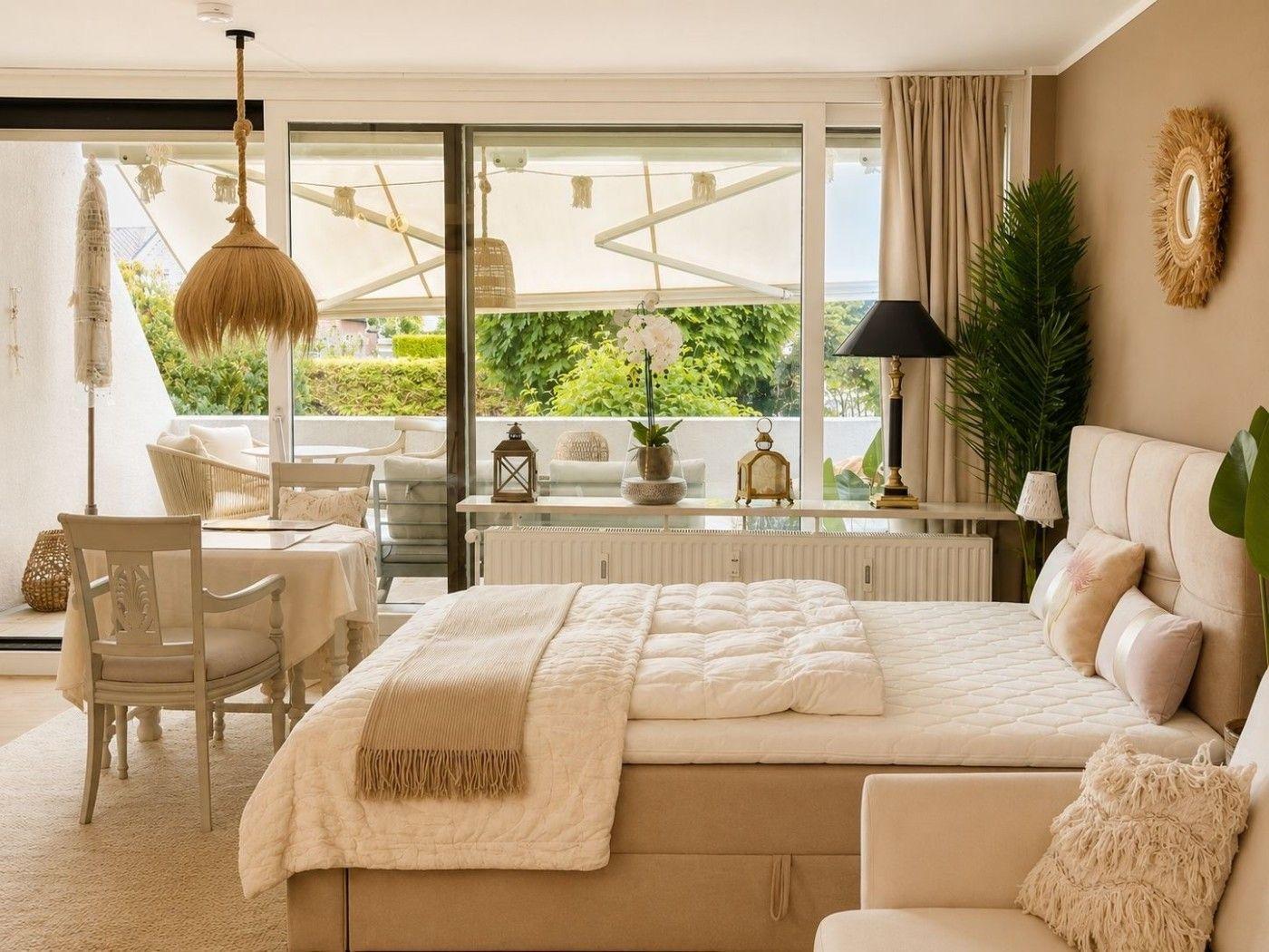 Schlafzimmer mit Bett, Tisch, Stühlen und Blick auf Balkon mit Garten.